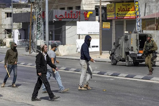 جندي إسرائيلي قرب مستوطنين في أحد شوارع الضفة الغربية (أرشيفية - وكالة «وفا»)