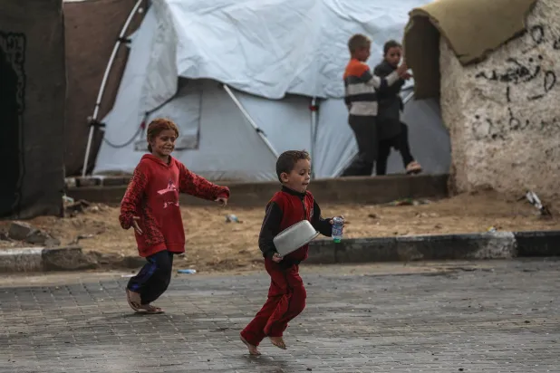 أطفال فلسطينيون يلعبون خارج مخيم في مدينة غزة (إ.ب.أ)