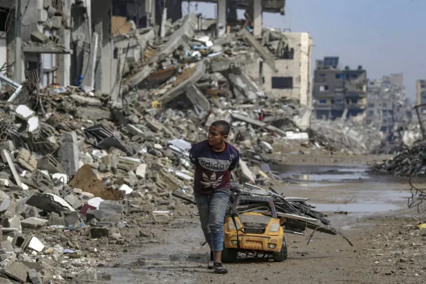 فتى فلسطيني يجمع قطع الحديد من بين أنقاض المباني في حي الشيخ رضوان بقطاع غزة (إ.ب.أ)