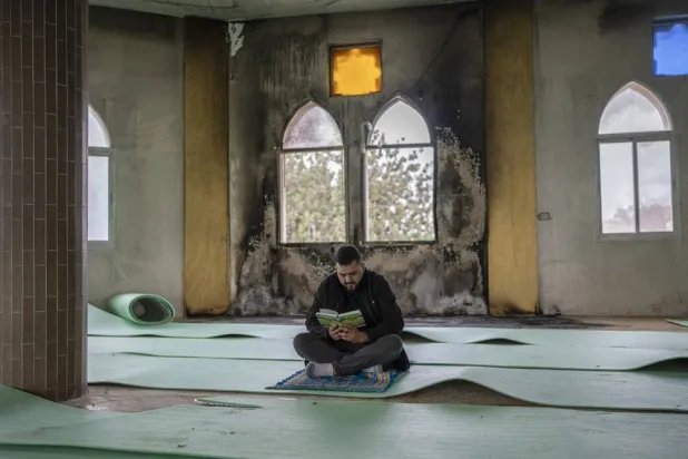  14 November 2025, Palestinian Territories, Salfit: A Palestinian man reads he holy Quran in front of a burned window before Friday prayer, inside the Hajjah Hamidah Mosque in the West Bank, one day after it was set on fire by Israeli settlers. (dpa)