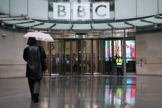A person walks with an umbrella outside BBC Broadcasting House, after Director General Tim Davie and CEO of BBC News Deborah Turness resigned on Sunday, November 9, following accusations of bias at the British broadcaster, including in the way it edited a speech by US President Donald Trump, in London, Britain, November 14, 2025. REUTERS/Isabel Infantes
