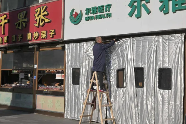 عامل يقوم بتركيب ستارة سميكة لفصل الشتاء في مجمع تجاري في بكين (أ.ف.ب)