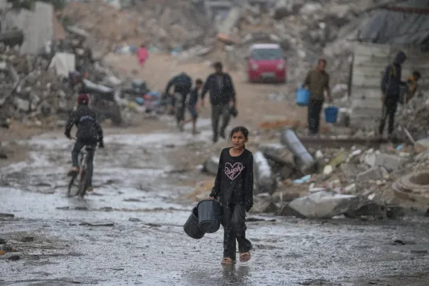 طفلة تحمل وعائين خاليين في طريقها لجلب المياه وسط أمطار غزيرة على حي الشيخ رضوان بمدينة غزة أمس (أ.ب)