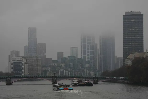  A catamaran (C) makes it way down the Thames towards high-rise buildings partly obscured by clouds in London on November 14, 2025, as inclement weather affects much of the country due to Storm Claudia. (AFP) 