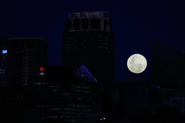 The moon rises between buildings in Sydney, Australia, Wednesday, Nov. 5, 2025. (AP Photo/Rick Rycroft)