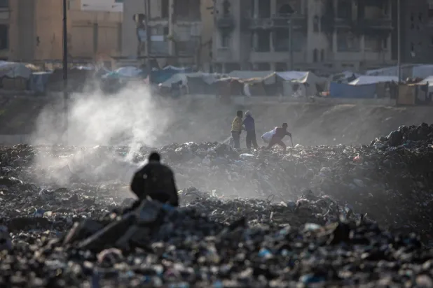 فلسطينيون يجمعون المخلفات البلاستيكية من بين أنقاض المباني في خان يونس بجنوب قطاع غزة (إ.ب.أ) 