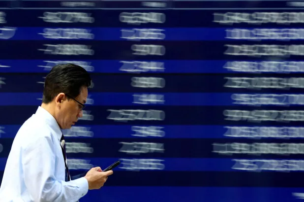 يمرّ رجل بجانب شاشة إلكترونية تعرض لوحة الأسهم في طوكيو (رويترز)