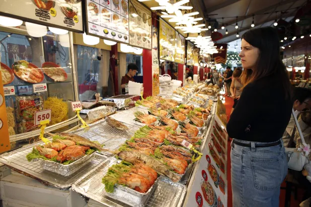 سائحة تشتري المأكولات البحرية بأحد أسواق بانكوك (إ.ب.أ)