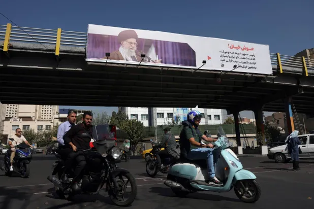 Iranians drive past a banner featuring a picture of Iranian Supreme Leader Ali Khamenei with a quote in Persian that reads, 'Cheerful! The US president is proud that they have destroyed and bombed our nuclear industry. Very well, keep dreaming,' hanging on a street in Tehran, Iran, 21 October 2025.  EPA/ABEDIN TAHERKENAREH