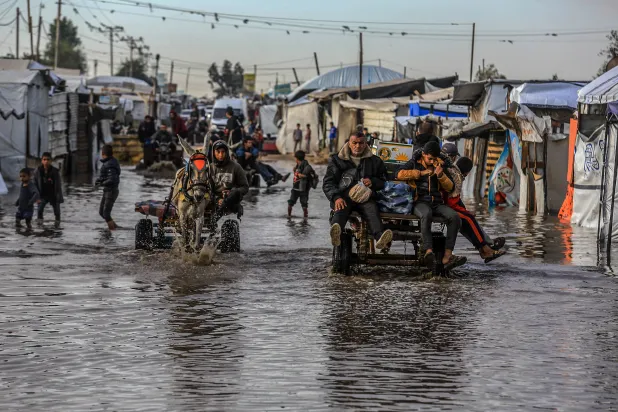 فلسطينيون يستخدمون عربات تجرها الحمير لعبور الشوارع الغارقة في ظل البرد القارس والأمطار الغزيرة بجنوب قطاع غزة (د.ب.أ)