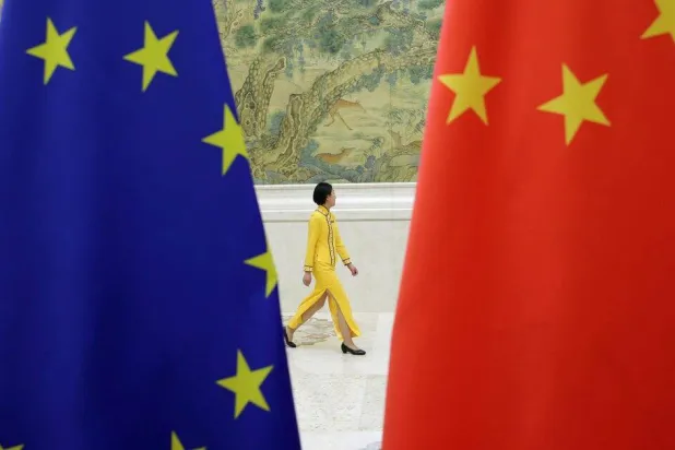 يمرّ أحد الموظفين أمام أعلام الاتحاد الأوروبي والصين في بكين (رويترز)