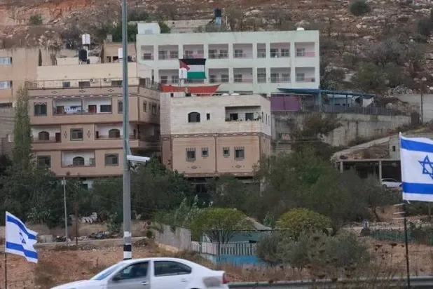 A Palestinian flag is seen on a building opposite Israeli national flags placed at the entrance of As-Sawiyah village, south of Nablus in the occupied West Bank, on November 16, 2025. (AFP)
