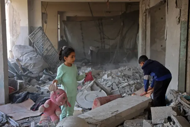 Gazze şehrinin ez-Zeytun mahallesinde yerinden edilmiş kişilerin barındığı bir binanın enkazı arasında oyuncaklarını taşıyan Filistinli bir kız çocuğu (AFP)