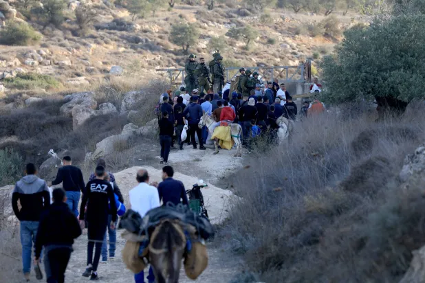 جنود إسرائيليون يراقبون مزارعين فلسطينيين في طريقهم لعبور بوابة للدخول إلى حقول الزيتون قرب مستوطنة آلون مور قرب قرية سالم بالضفة الغربية المحتلة (إ.ب.أ)