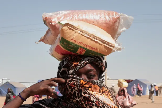 A Sudanese woman displaced from El-Fasher carries sacks of food aid on her head at the newly established El-Afadh camp in Al Dabbah, in Sudan's Northern State, Sunday, Nov. 16, 2025. (AP Photo/Marwan Ali)