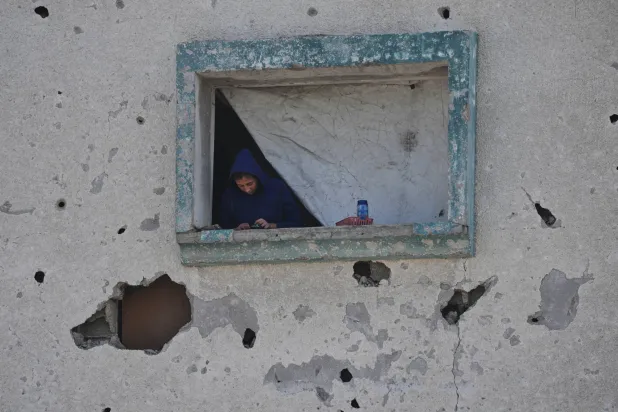 فلسطينية تنظر من نافذة بيتها المتضرر في جباليا بقطاع غزة الجمعة (أ.ب)