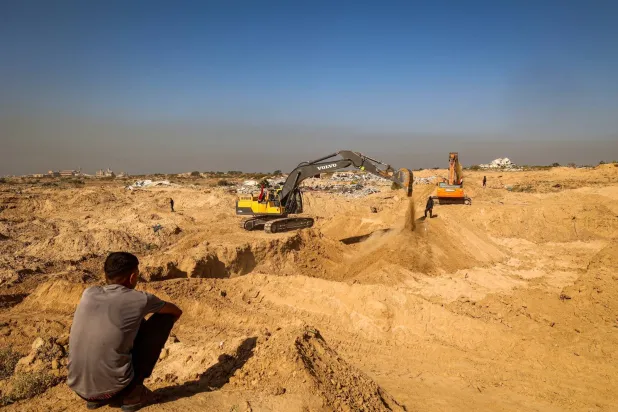 فلسطيني يراقب عناصر من حركة «الجهاد الإسلامي» وهم يبحثون عن جثث في النصيرات بغزة (أ.ف.ب)