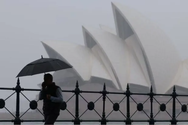 رجل يحمل مظلة يمر أمام دار الأوبرا في سيدني بأستراليا... 21 نوفمبر 2024 (رويترز)