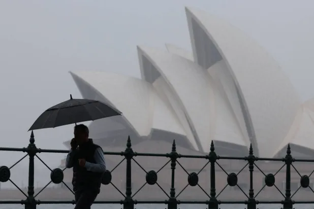 A man carrying an umbrella walks past the Sydney Opera House in Sydney, Australia, November 21, 2025. REUTERS/Hollie Adams