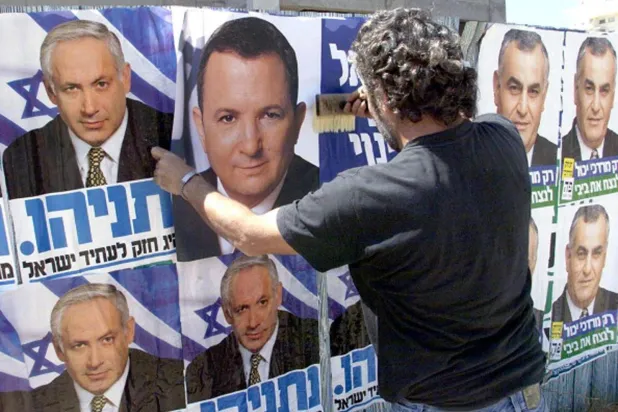 رجل يضع ملصقاً انتخابياً لإيهود باراك فوق صورة المرشح بنيامين نتنياهو في انتخابات 1999 (غيتي)
