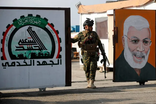 یک نیروی «الحشد الشعبی» در حال نگهبانی از دروازه‌ای در بغداد است که تصویر ابومهدی المهندس بر آن نصب شده است  (AFP)