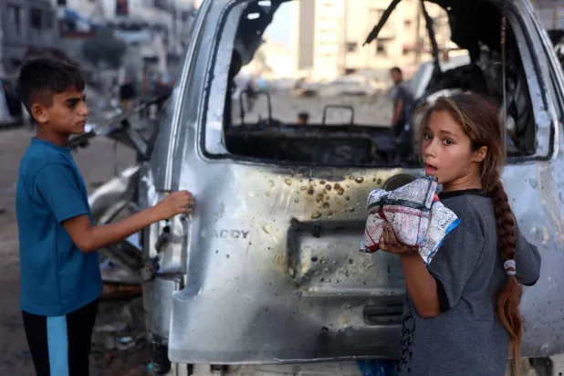 طفل وفتاة فلسطينيان ينظران إلى سيارة استهدفتها قوات الجيش الإسرائيلي في مدينة غزة (أ.ف.ب)