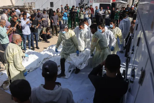 موظفو مستشفى ناصر يستخرجون رفات فلسطينيين مجهولين من شاحنة مبردة في خان يونس بعد أن أعادتهم إسرائيل بموجب اتفاق وقف إطلاق النار (أ.ف.ب)