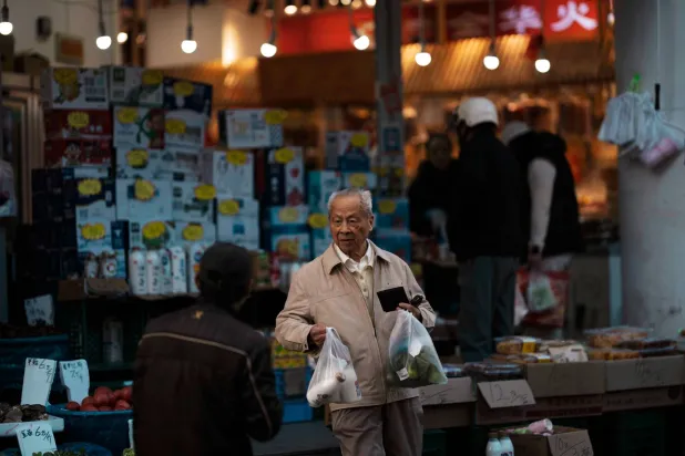 رجل مسن يحمل أكياساً أثناء خروجه من متجر بقالة في شنغهاي بالصين (إ.ب.أ)
