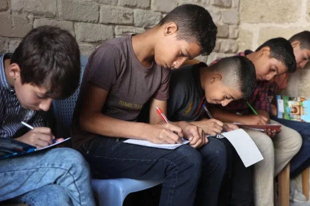 Palestinian children take notes as they attend a class in the historic Al-Kamaliya al-Othmanya school in Gaza City's Old Town, as part of a volunteer initiative organized by displaced teachers, in Gaza City. Omar AL-QATTAA / AFP/File
