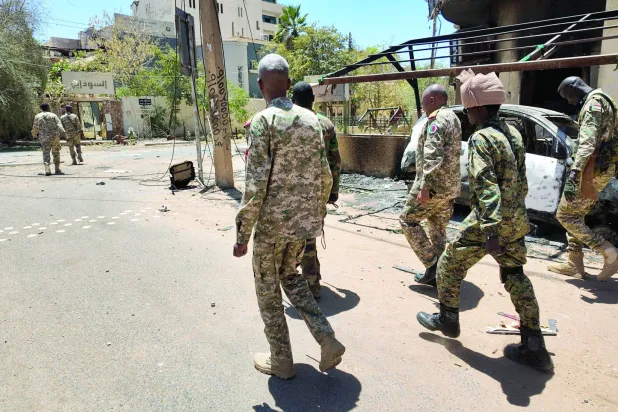 أفراد من الجيش السوداني يسيرون بجوار مركبات عسكرية مدمرة في الخرطوم (رويترز)