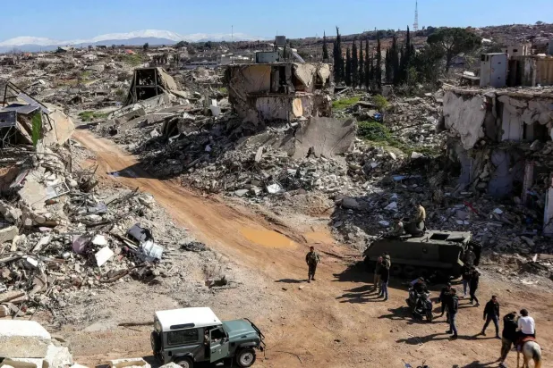 Residents of Kfarkela gather beside Lebanese army vehicles deployed over the ruins of a destroyed building in the southern village (AFP)