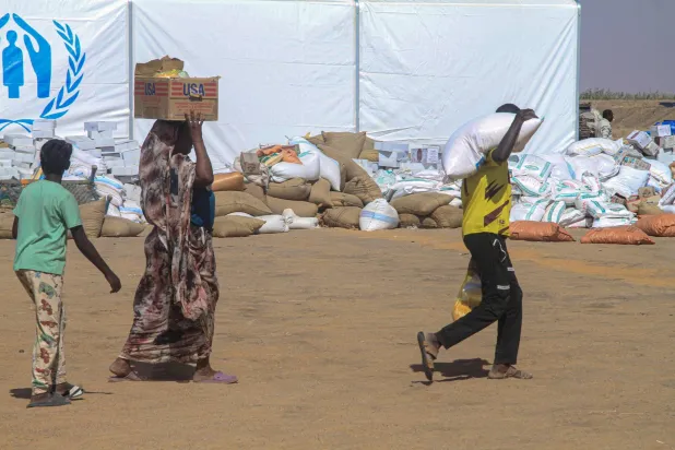 Sudanese people who fled El-Fasher carry humanitarian aid after receiving it at the Al-Afad camp for displaced people in the town of Al-Dabba, northern Sudan, on November 25, 2025. (Photo by Ebrahim HAMID / AFP)