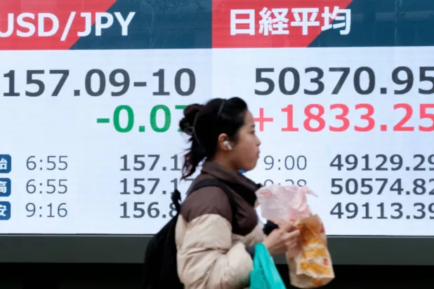 سيدة تمر أمام شاشة تعرض حركة الأسهم والعملات في وسط العاصمة اليابانية طوكيو (أ.ف.ب)