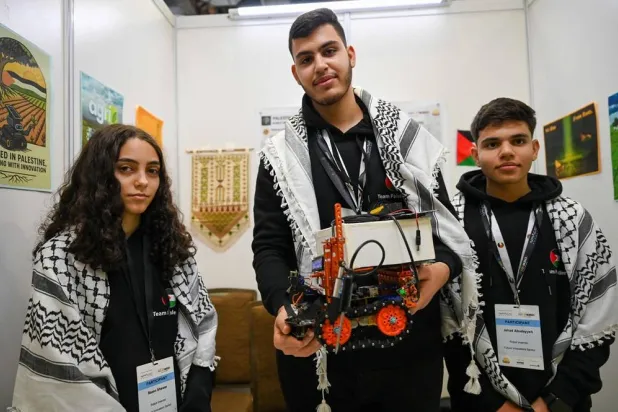 Palestinian participants Razan Shawar (L), Jehad Abudayyah (R), and Mustafa Assi (C) pose with their robot design for the Future Innovators category at the World Robot Olympiad in Singapore on November 28, 2025. (AFP) 