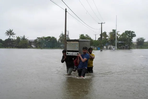 أشخاص يحملون ثلاجة ويخوضون الشارع المغمور بالمياه بعد هطول أمطار غزيرة في ويلامبيتيا بسريلانكا (رويترز)