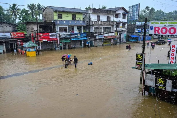 People wade through a flooded road after heavy rainfall in Kaduwela on the outskirts of Colombo on November 28, 2025.  (Photo by Ishara S. KODIKARA / AFP)