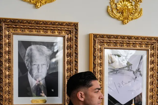 أحد عناصر الخدمة السرية يقف أمام صور للرئيس دونالد ترمب وأخرى للتوقيع الآلي للرئيس السابق جو بايدن في ممشى المشاهير الرئاسي في رواق البيت الأبيض (أ.ب)