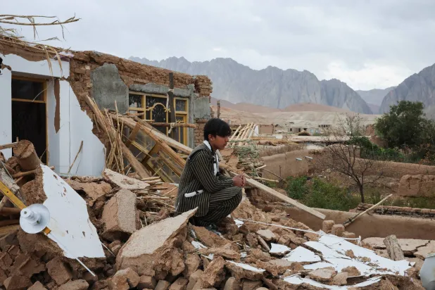 A boy sits next to his damaged house, in the aftermath of an earthquake, in Samangan province, Afghanistan, November 4, 2025. REUTERS/Sayed Hassib