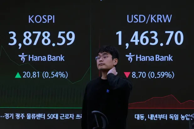 يمرّ متداول عملات بجوار شاشة تُظهر مؤشر «كوسبي» إلى اليسار وسعر صرف الدولار الأميركي بمقرّ بنك هانا في سيول (أ.ب)