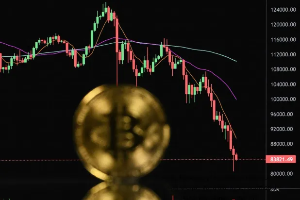 An illustration photograph taken on November 22, 2025, shows a gold plated souvenir Bitcoin coin reflected in a mirror and arranged for a photograph in front of a computer screen displaying the Bitcoin monthly price chart in a residential property in Guildford, south of London. (Photo by Justin TALLIS / AFP)