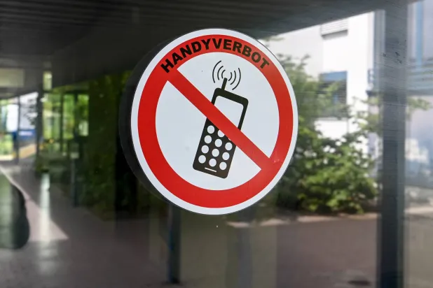 FILED - 22 August 2022, Berlin: A "no cell phones" sign is posted at the entrance to a school in Neukoelln, Germany. Photo: Jens Kalaene/dpa