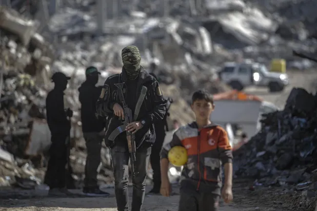 طفل فلسطيني يقف خلفه مقاتلون من «كتائب القسام» التابعة لـ«حماس» أثناء بحثهم عن جثث رهائن إسرائيليين في مخيم جباليا شمال غزة يوم الاثنين (إ.ب.أ)