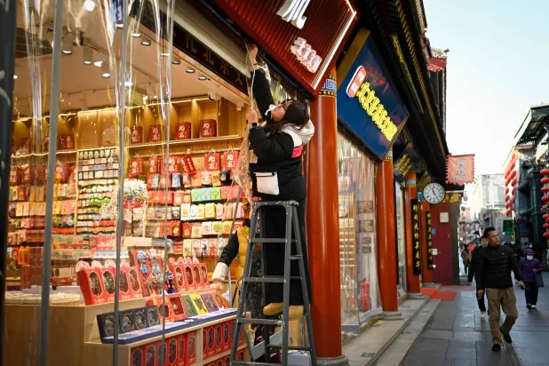 سيدة تعلق حاجزاً للأمطار على متجرها في حي تجاري بوسط العاصمة الصينية بكين (أ.ف.ب)