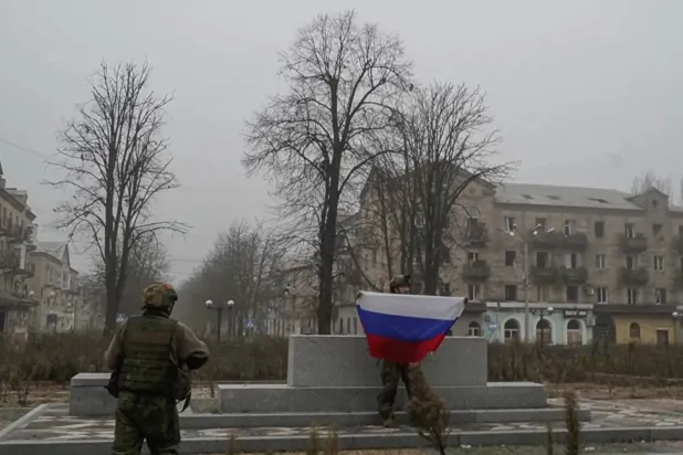 جندي روسي يرفع علم بلاده في إحدى البلدات بإقليم دونيستك الأوكراني الثلاثاء (إ.ب.أ)