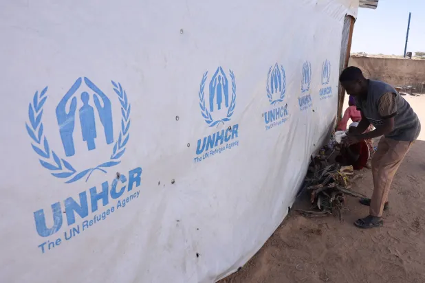 Ibrahim Mohamed Ishaq, 35, a Sudanese refugee father from el-Fasher, stands near firewood after purchasing it for warmth inside the Tine transit camp, after arriving and securing a place in eastern Chad, as he and his family flee ongoing clashes between the paramilitary Rapid Support Forces (RSF) and the Sudanese army, November 22, 2025. (Reuters) 