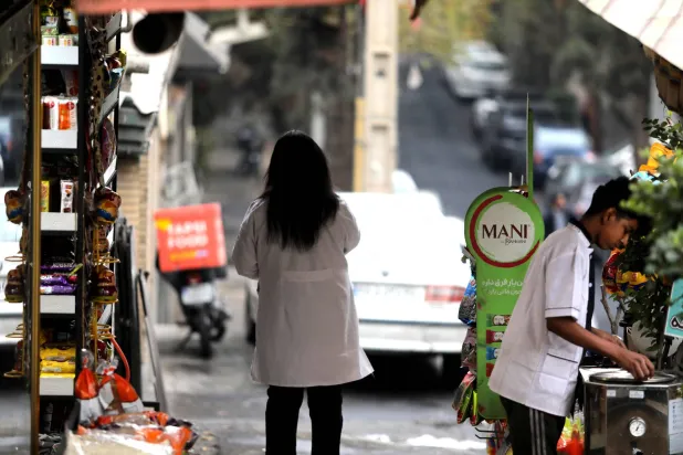 A woman stands under a canopy waiting for the rain to stop, as the first winter rains arrive following one of the driest years on record, in Tehran on December 1, 2025. (Photo by ATTA KENARE / AFP)