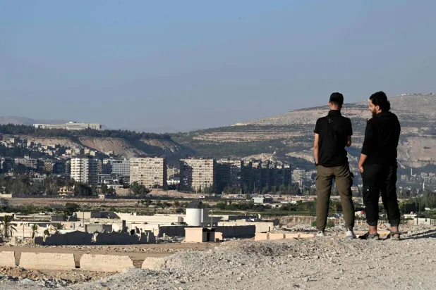 شابان سوريان يقفان على تلة في داريا مُطلّة على القصر الرئاسي الفسيح للرئيس السابق بشار الأسد في دمشق أواخر أكتوبر الماضي (أ.ف.ب)