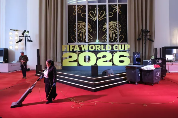 عامل نظافة ينظّف السجادة الحمراء بجوار لافتة كُتب عليها: «قرعة كأس العالم 2026» في مركز كيندي بواشنطن (د.ب.أ)