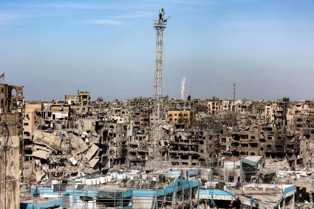 رجل يعلق علماً فلسطينياً على هوائي في مبنى شبه مدمّر كان يضم عيادة لـ«الأونروا» في مخيم جباليا بغزة (أ.ف.ب)