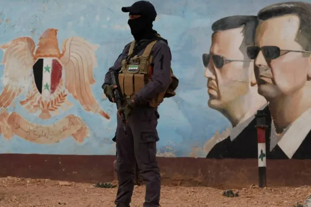 A member of Hayat Tahrir al-Sham stands guard near an image of Syria's Bashar al-Assad at the fourth division headquarters in Damascus, Syria, January 23, 2025 (Reuters)